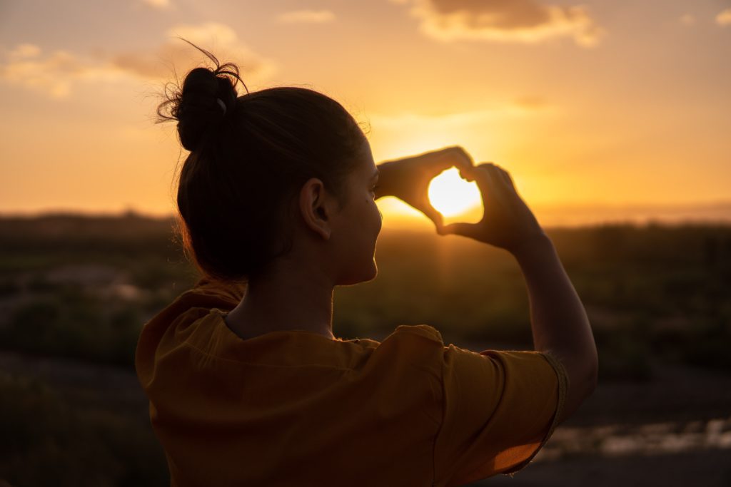 making heart shape with hands at sunset